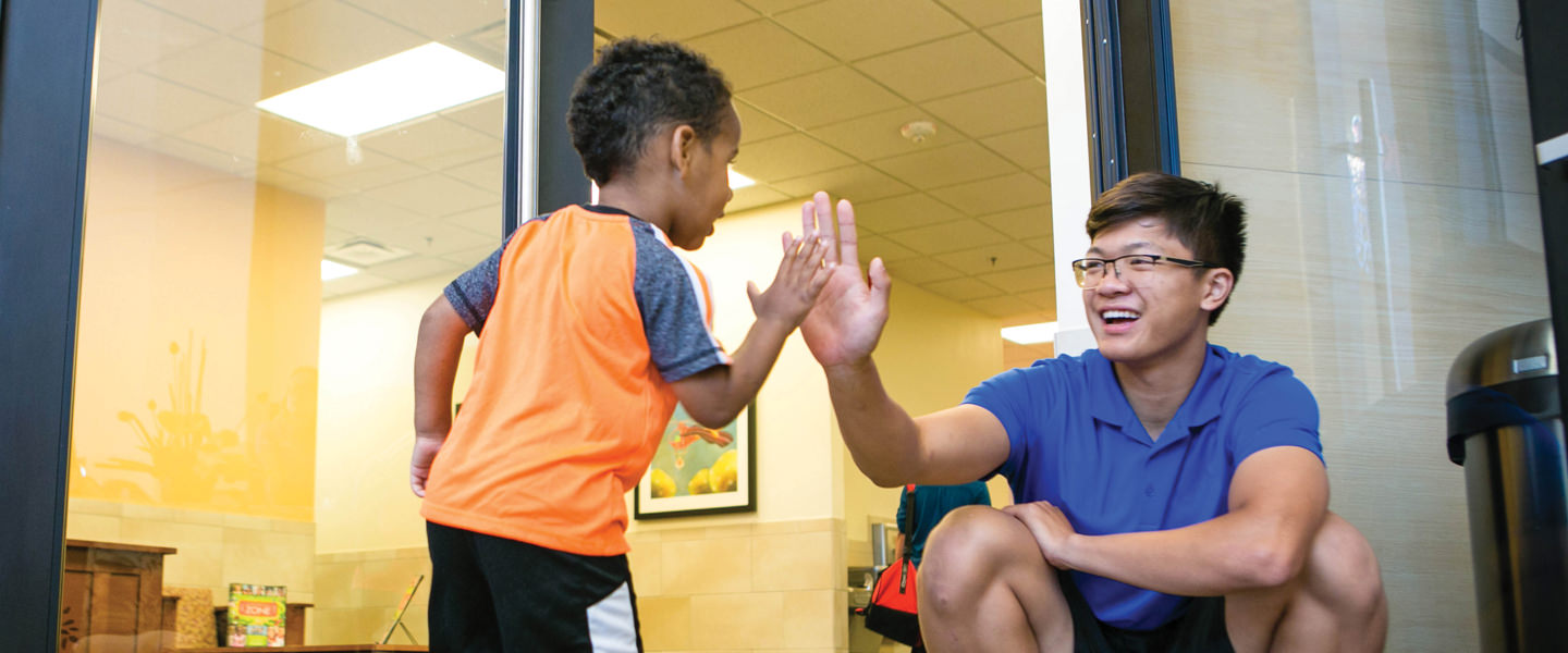 Kid high-fiving Kids Club staff member on their way into the club